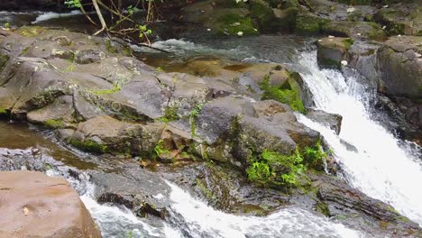 HD-Hawaii-Kauai-Zeitlupe-Nach-Rechts-Schwenken-Und-Nach-Unten-Kippen,-Geteilter-Wasserfall-Mit-Lavagestein-Im-Vordergrund-Am-Grund-Des-Wasserfalls