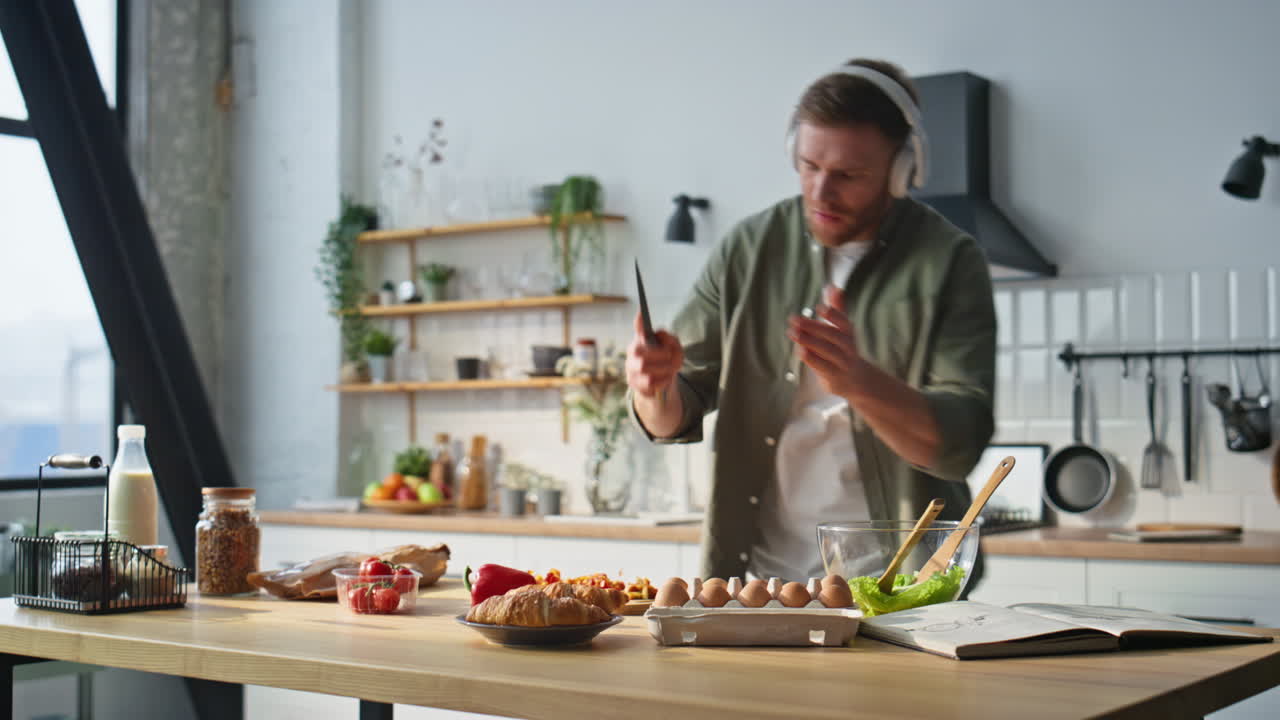 Singing man chopping pepper in kitchen apartment wearing earphones. Cheerful guy