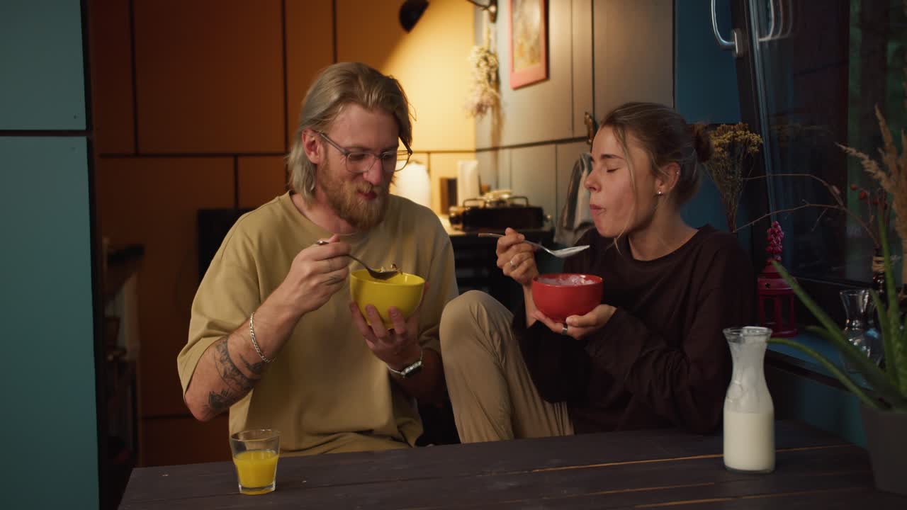 Happy couple girl and guy stoles sit in the kitchen in the morning and eat cereal with milk in a cozy room