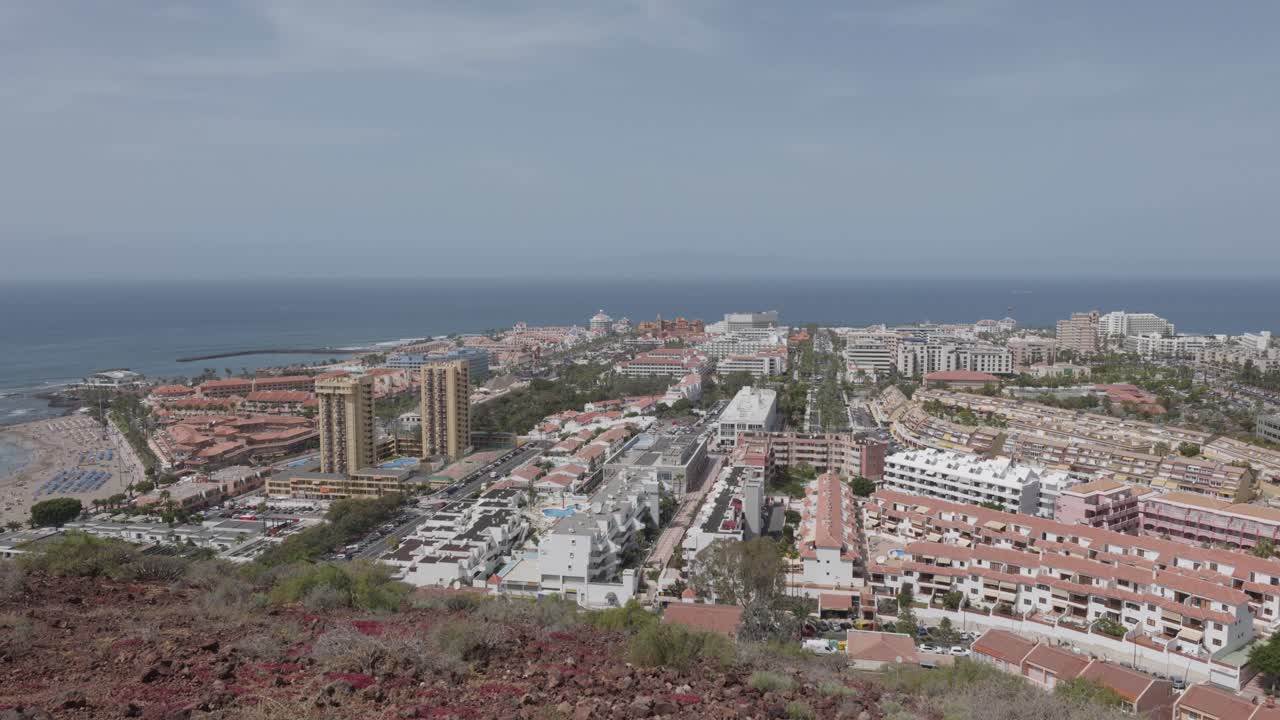 View of a coastal town with palm trees and hotels next to the ocean in Playa de Las Americas, Tenerife, Canary Islands, Spain.