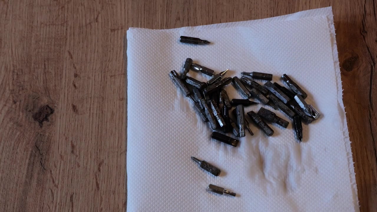 Mano maschile che asciuga e pulisce piccole punte da trapano per cacciavite in metallo usando un tovagliolo di carta bianco su un banco da lavoro in legno