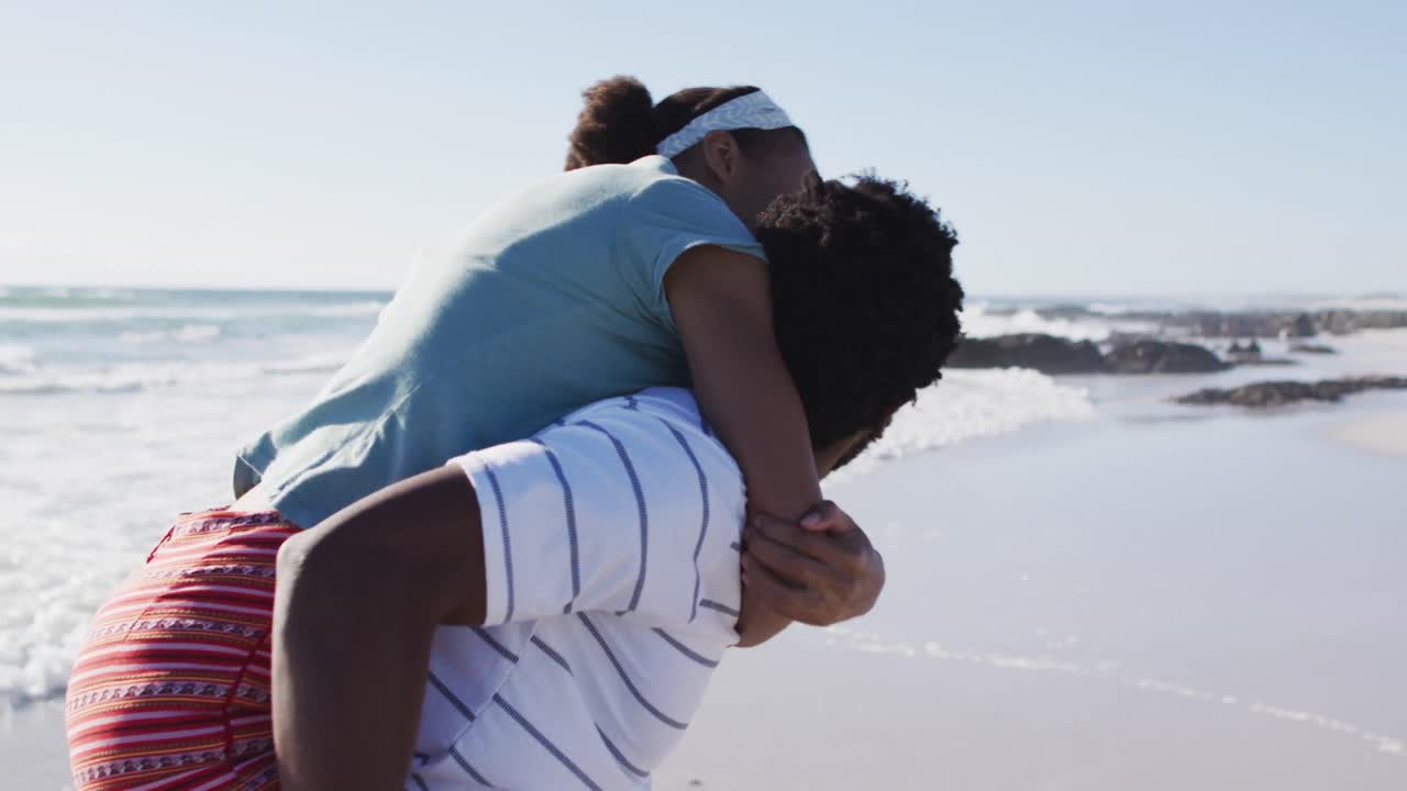 Afroamerikansk mand bærer afroamerikansk kvinde på ryggen på stranden