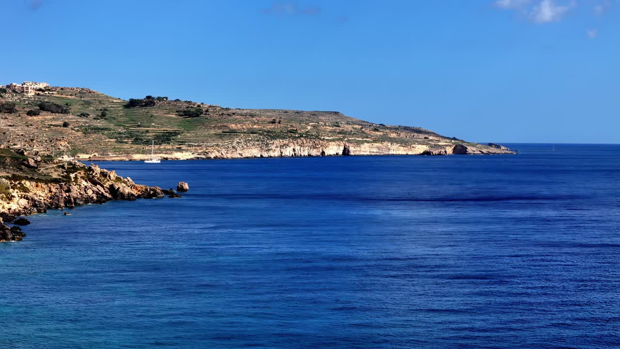 Vista mozzafiato con grandangolo della frastagliata costa maltese in una soleggiata giornata estiva, che mette in mostra il vivace mare blu Mediterraneo che incontra le dorate scogliere rocciose sotto un cielo limpido nelle isole di Gozo