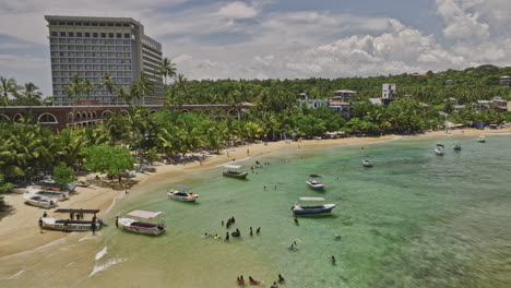 Unawatuna-Sri-Lanka-Aerial-v6-low-drone-fly-along-sandy-beach-coastal-shore-capturing-tropical-beachfront-resorts-and-hotels,-and-hillside-Yaddehimulla-views---Shot-with-Mavic-3-Cine---April-2023