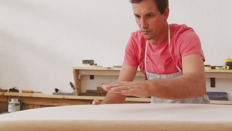 fabricante de tablas de surf caucásico chequeando una tabla de surf de madera antes de pulirla