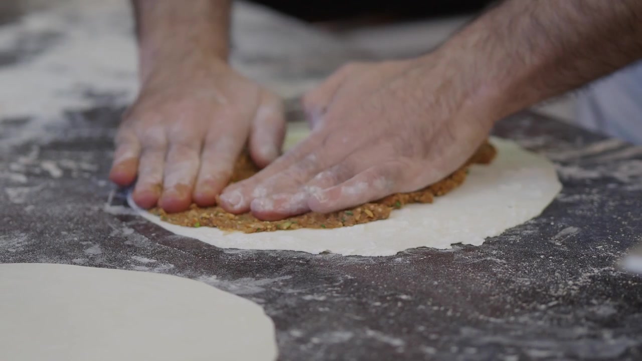 Chef che spalma un composto di carne sull'impasto per una focaccia tradizionale
