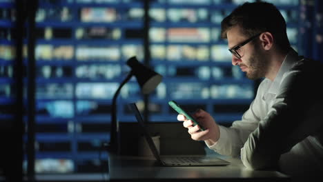 Office-Building-with-Businessman-Using-Mobile-Phone-and-Standing-by-the-Office-Window.-Man-working-in-modern-office-late-at-night.-Busy-caucasian-manager-at-work-with-mobile-telephone.