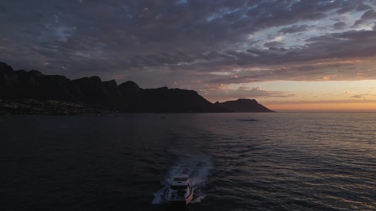 Betagende solnedgang over havet, der panorerer mod De Tolv Apostle bjerge i Cape Town, med en båd på havet.