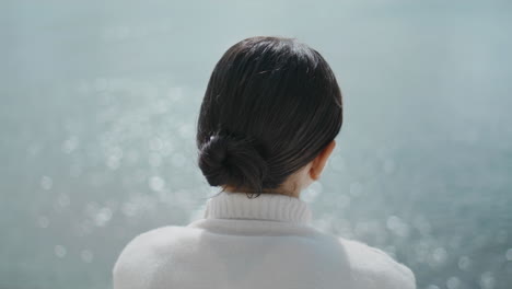 무선 이어폰으로 음악을 듣고 있는 관광객 여성이 호수 물 에 앉아 있습니다.