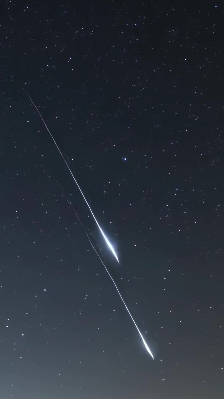 Vertical video: Entering upper-left, fireball splitting and streaking down over stars, horizon glow