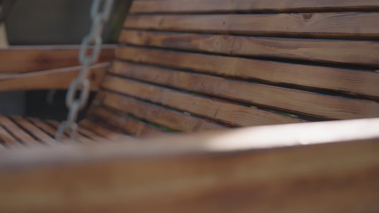 Close up of polished wooden swing arm in warm sunlight, with chain support softly blurred in background, highlighting natural wood grain, craftsmanship details, and smooth texture in backyard