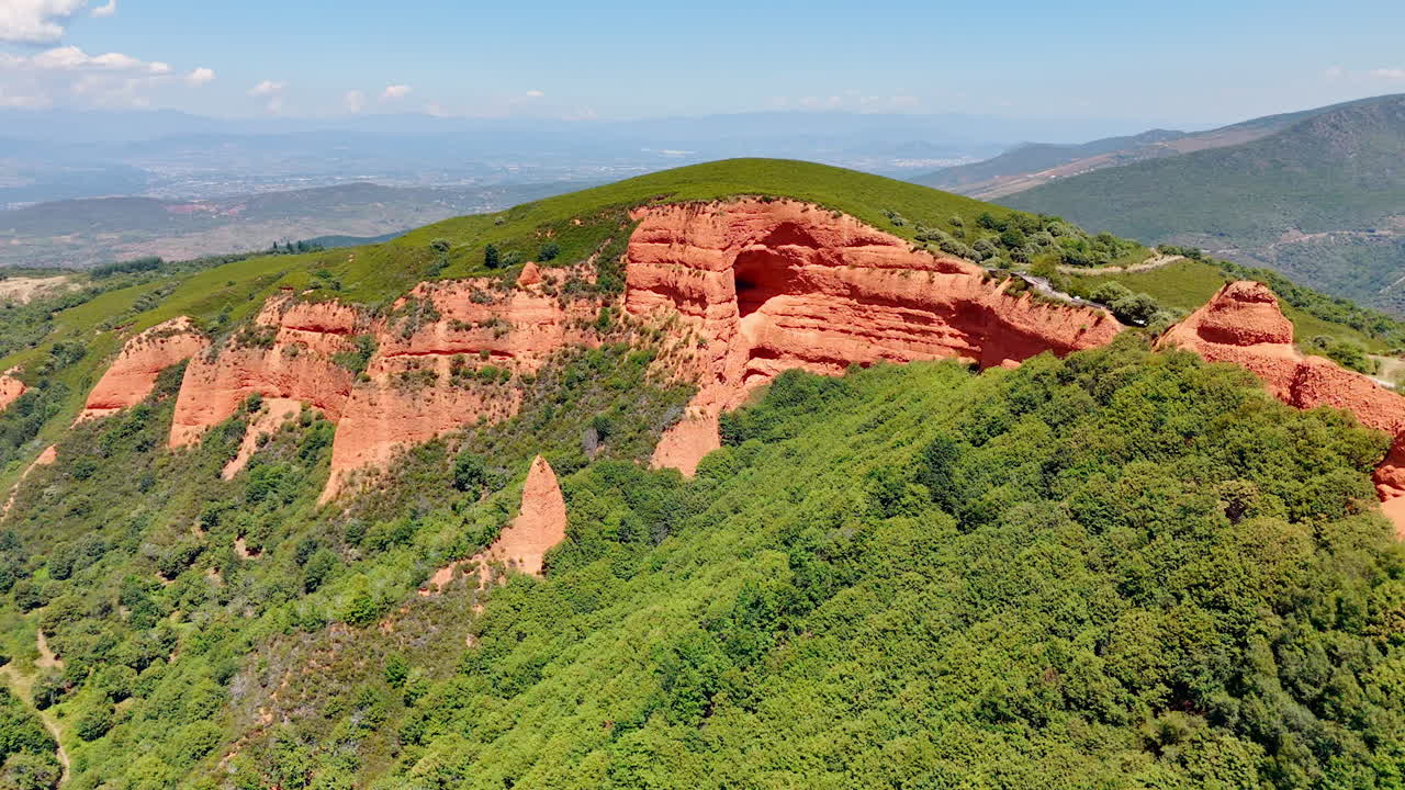 Approaching red rock formations sticking out of greenery. Drone footage above the splendid mountainous landscape on sunny day.