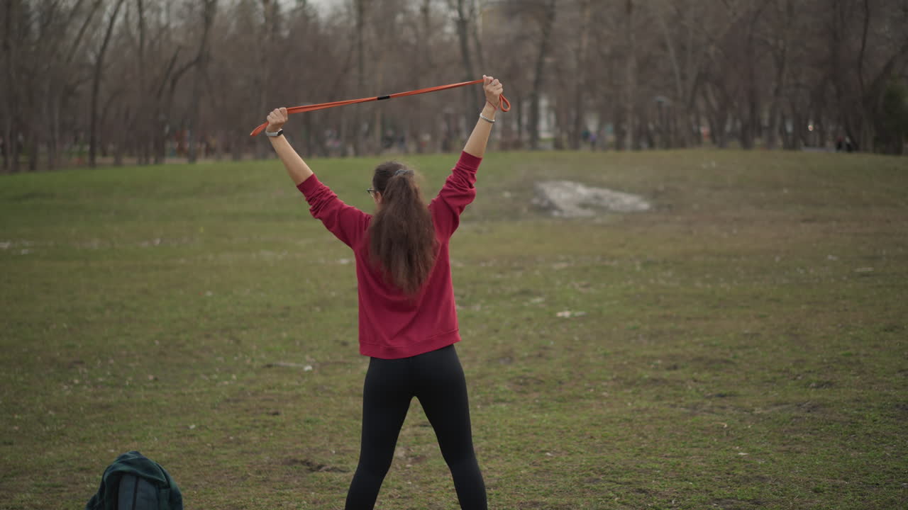 Caucasian Woman Performing Lateral Stretches With Ribbon Prop In Park. Sweeping Side Bends, Active Stance, Nearby Historic Building And Cool Light Create Dramatic Training Sequence