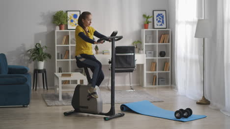 fotografía completa de la sala de estar con equipos deportivos mujer joven está entrenando en bicicleta de ejercicio entrenamiento y estilo de vida saludable acondicionamiento físico en el hogar