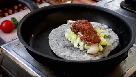 cooking chicken taco series: close-up of chef's hand wearing gloves putting salsa sauce and sliced tomato onto flour tortilla in a frying pan