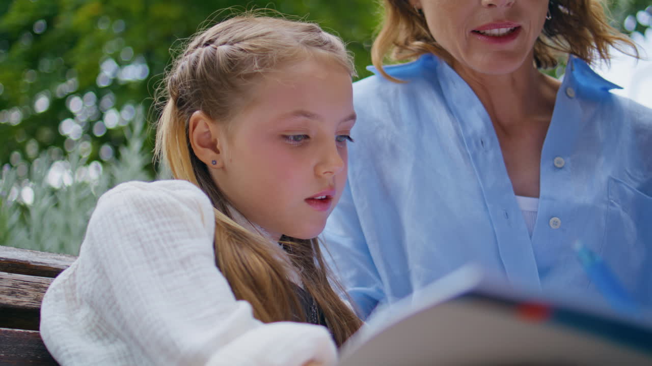 Closeup pensive schoolgirl writing copybook with mom at park. Kid holding pen