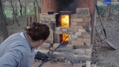 handheld shot of a potter tending to the fire in her kiln to maintain appropriate temperatures