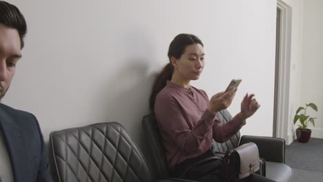 female candidate wearing suit in office waiting for job interview looking at mobile phone 1