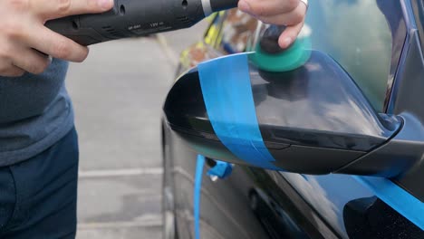 polishing a black car mirror with a small machine polisher