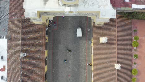 aerial view following a tuktuk driving under the santa catalina arch in sunny antigua, guatemala - top down, drone shot