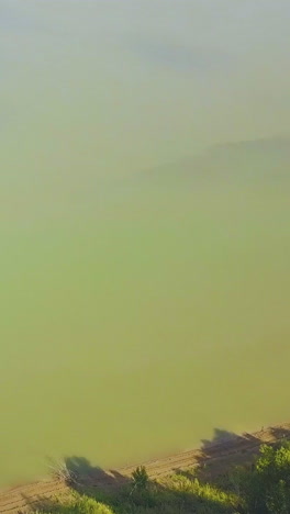 round aerial view from couple on high steep bank over green tranquil river with flying bird to distant town on sunny day