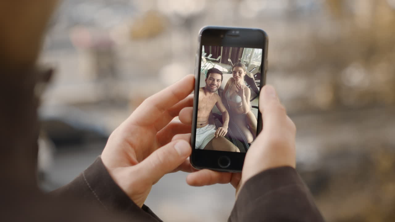 Primo piano di un uomo che effettua una videochiamata con gli amici tramite smartphone. Persone sorridenti partecipano a una conferenza