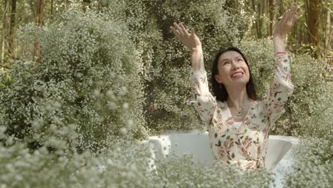 An-attractive-young-Asian-woman-sits-in-a-garden-tub-and-admires-the-beautiful-white-blossoms-all-around-her