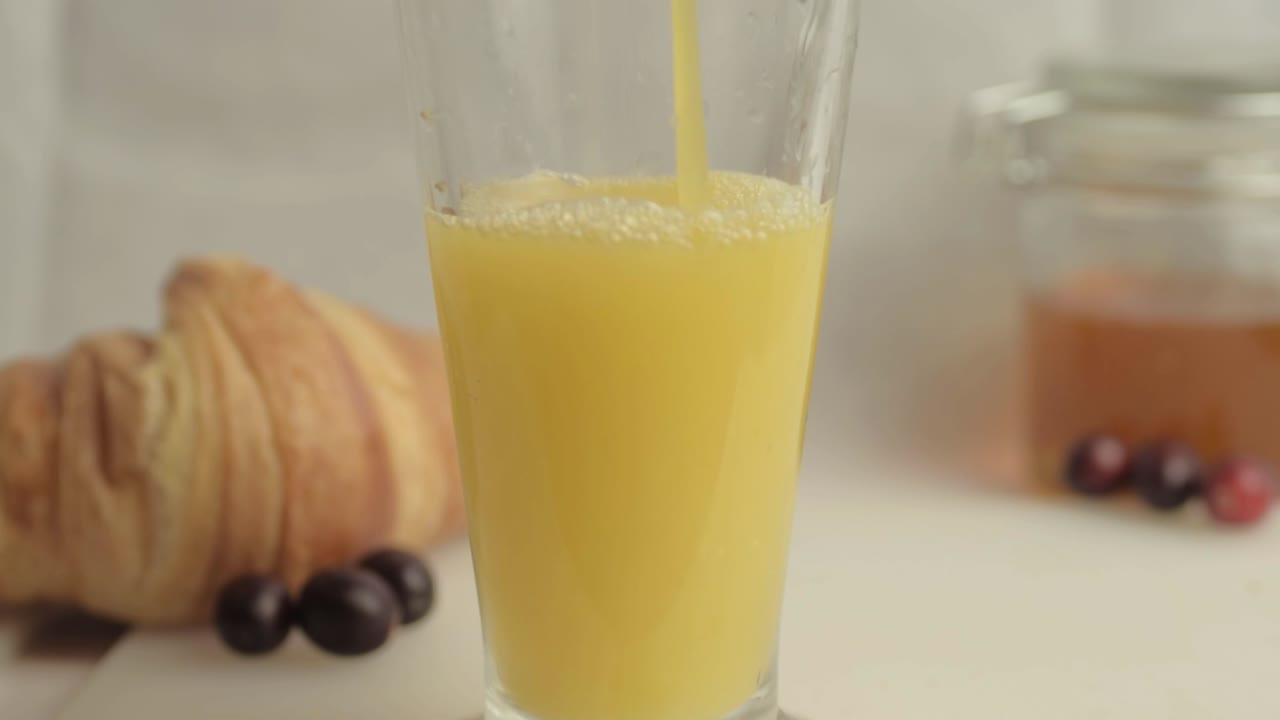 vertiendo jugo de naranja fresco en el desayuno con miel y croissants