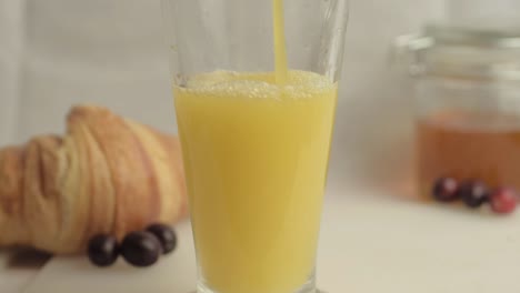 vertiendo jugo de naranja fresco en el desayuno con miel y croissants