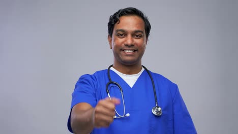 Happy-Indian-Male-Doctor-Showing-Thumbs-Up.healthcare,-profession-and-medicine-concept-happy-smiling-indian-doctor-or-male-nurse-in-blue-uniform-showing-thumbs-up-over-grey-background