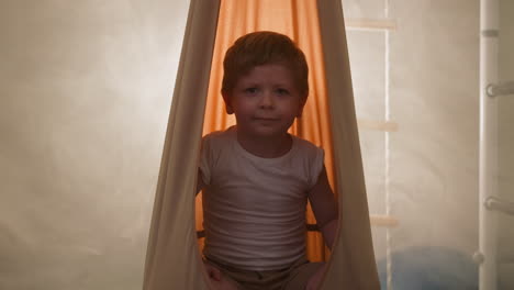 Little-boy-sits-in-orange-hammock-illuminated-with-light