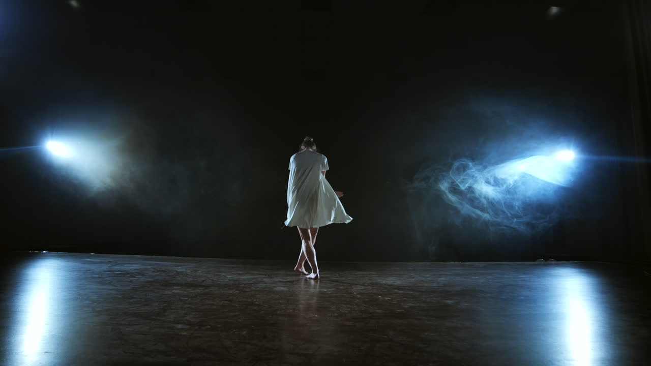 Dançarina moderna em um vestido branco curto executa danças expressivas, belas e dramáticas, correndo pelo palco, caindo no chão e girando. Lanternas e fumaça.