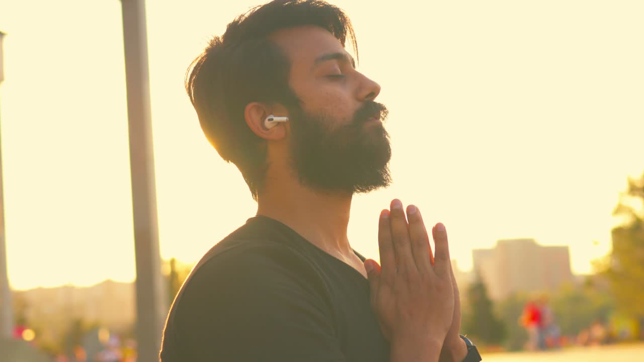 hombre barbudo con camiseta de algodón negro calentándose al aire libre en el parque de verano a la luz dorada del atardecer.