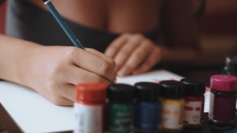 close up shot of young woman sitting at wooden table at home and drawing on a sheet of paper with a pencil