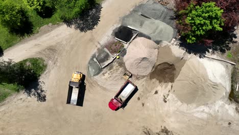 Empty-dump-trucks-next-to-sand-stockpiles,-aerial-top-down-rotate