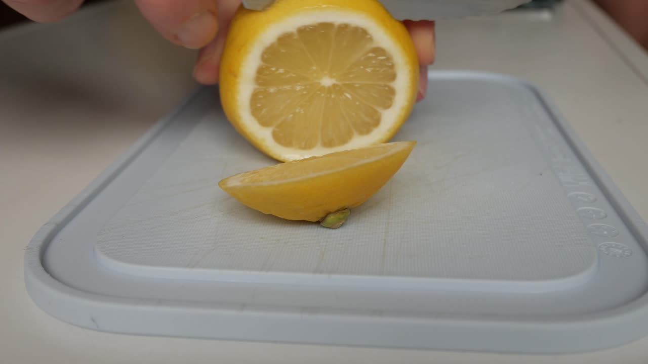 Fresh lemon being sliced with a knife on a white cutting board, preparation for lemonade