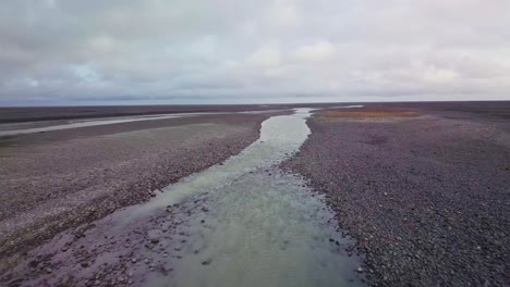 Flyover-above-chalky-glacial-river-flowing-through-Iceland