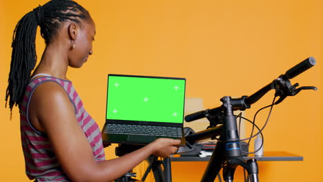 mujer alegre siguiendo videos tutoriales en la computadora portátil chroma key, aprendiendo a arreglar la bicicleta