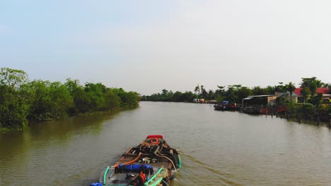 volando sobre el canal del delta del mekong en vietnam asia, transbordador flotando en el agua a lo largo de la vía fluvial por la orilla del río, ubicación turística de los barcos y tierras cubiertas de árboles verdes a lo largo de la orilla del río