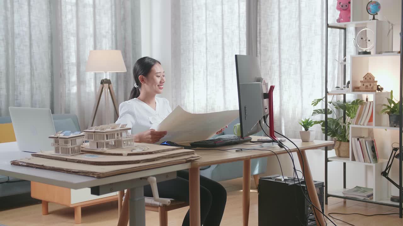 집 모델을 열고 집에서 데스크에서 작업하는 동안 청사진을 보는 아시아 여성 엔지니어