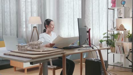 アジアの女性エンジニアが自宅のデスクトップで作業している間ブループリントを開けて見ています