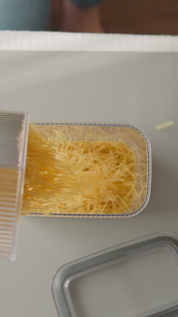 manos femeninas con manicura limpia verter espagueti crudo en un recipiente de plástico en cámara lenta. joven ama de casa cocina la cena en la cocina de casa vista superior