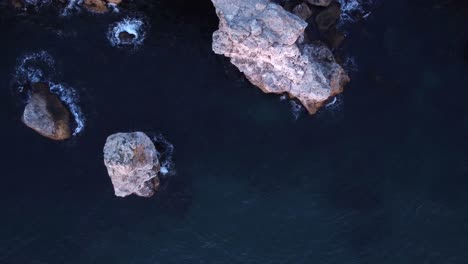 top down aerial view of waves splash against rocky seashore, background