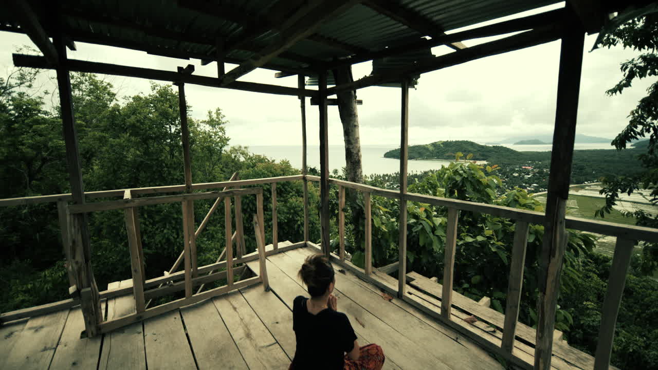 Woman meditating on a wooden platform with an ocean view