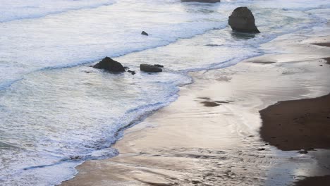 waves hitting rocks on a sandy beach