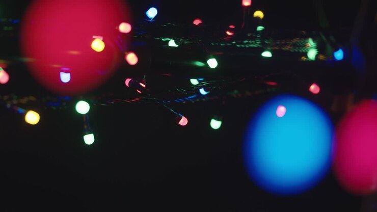 Many blurry glowing colourful lights of led holiday garlands shining in darkness of night. Abstract festive background.