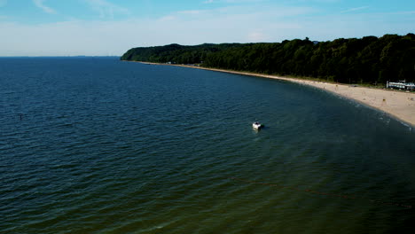 Vista-Aérea-Del-Barco-En-El-Mar-Báltico-Con-Paisaje-Forestal-Y-Playa-De-Arena-En-Gdynia,-Polonia