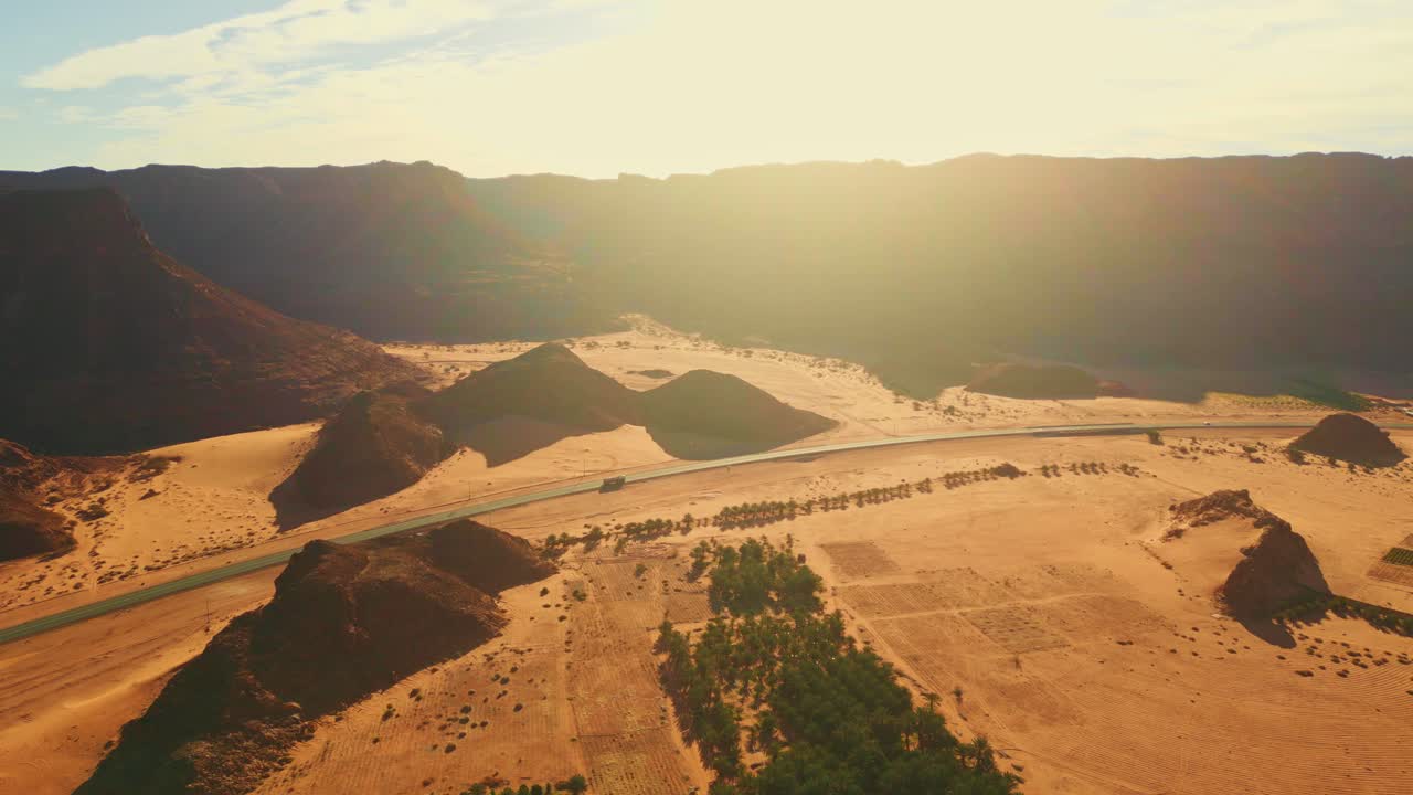 초록색 종려나무와 함께 사막을 가로질러 아스팔트 도로에 가운 교통이 있는 고속도로, 해가 지면 오렌지색 바위 산과 노란색 모래가 있는 협곡