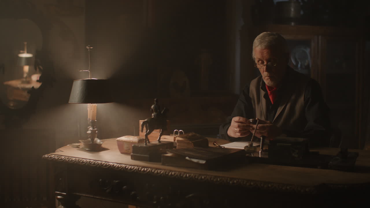 Older passionate man evaluates an old silver skull watch in his office at night