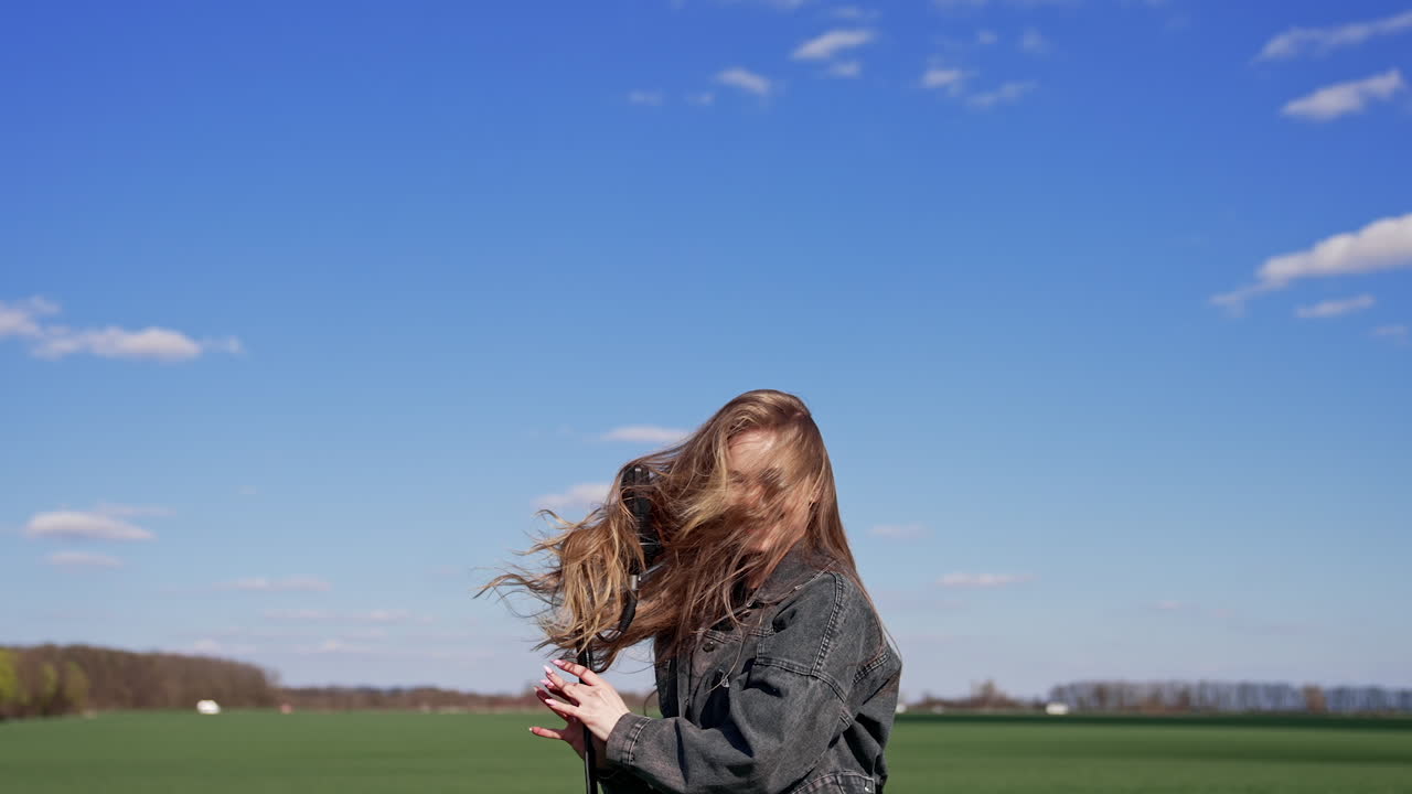 Singer moving her head near the microphone in nature. Attractive girl singing and dancing on green field under blue sky.